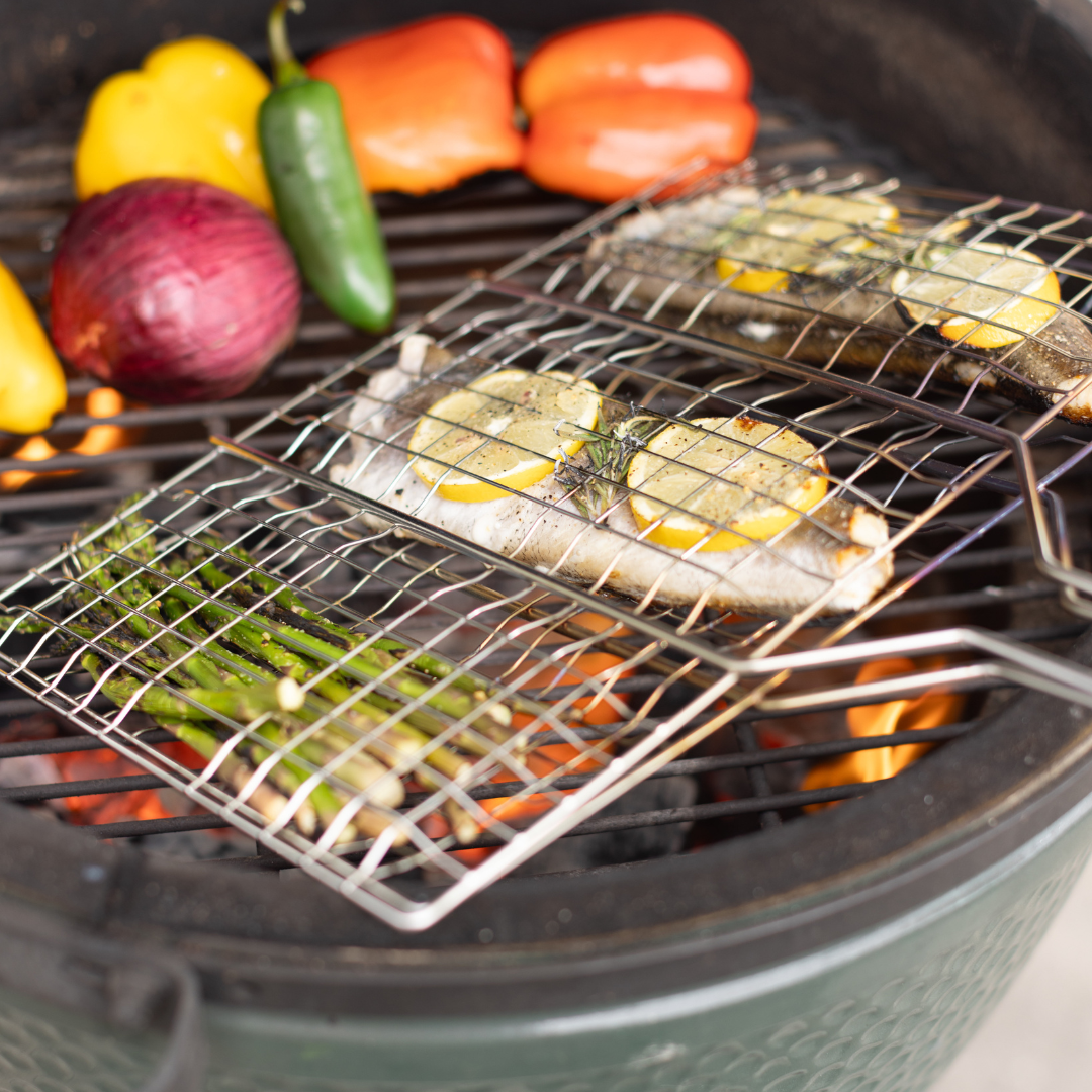 Whole fish with lemon and asparagus cook in the Barbecue Grill Basket over open flames, while roasting bell peppers, red onion, and jalapeño nearby—delicious additions to your BBQ menu.