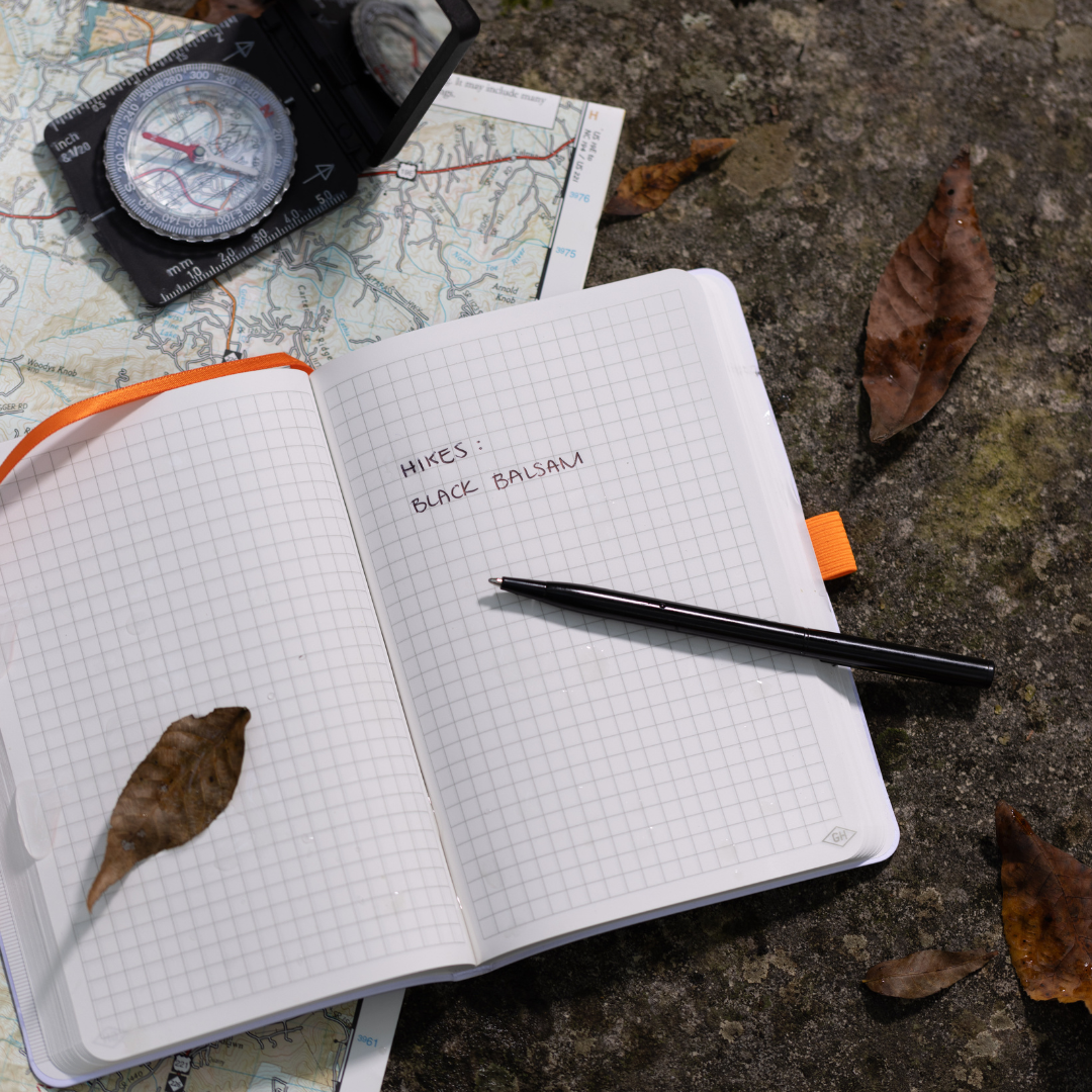 The Waterproof Notebook, open on a map with a compass and leaves nearby, features Hikes: Black Balsam inside—ideal for jotting pocket notes outdoors.