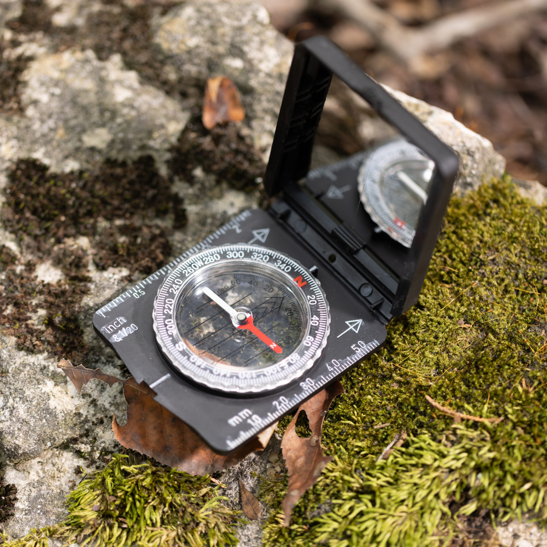 The Explorer Kit, featuring a handheld compass with a mirror, rests on a mossy rock among fallen leaves, inviting you to begin your next outdoor adventure.