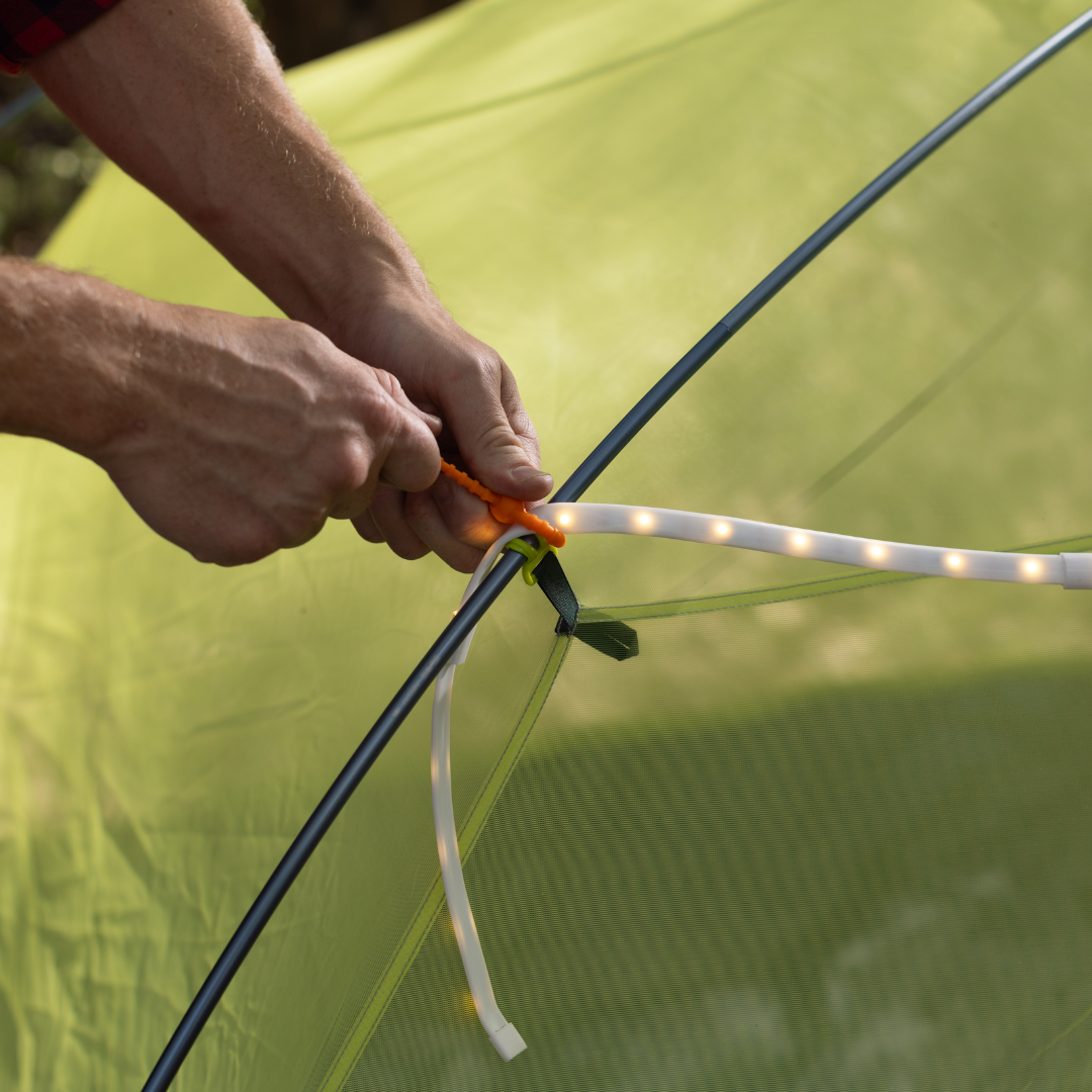 Close-up of hands attaching LED Rope Lights, a USB powered flexible light strip, to the inside frame of a green tent for convenient campsite lighting.