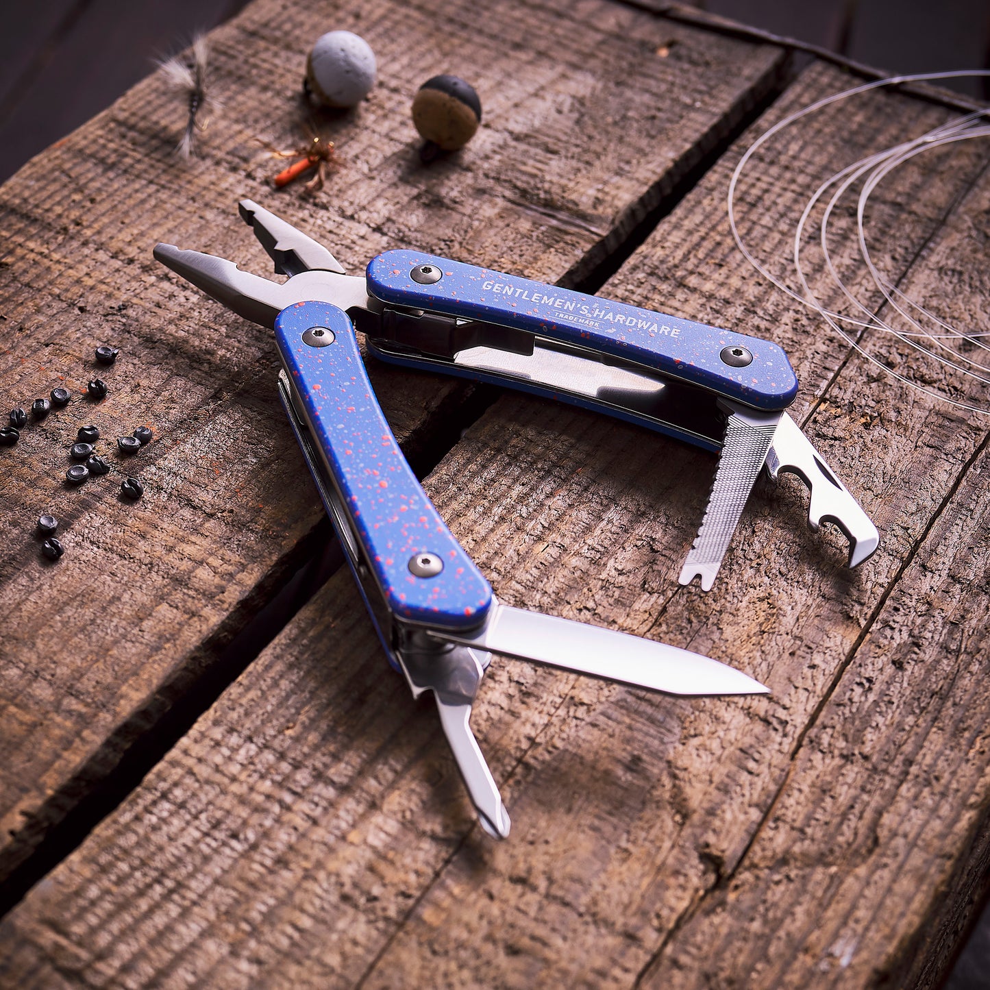 A Fishing Multi Tool with several open tools, including needlenose pliers, sits on a wooden surface next to fishing tackle, wire, and split shot weights.