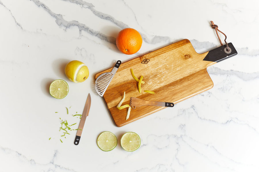 Compact bar tools surrounded by fruit and a cutting board. 