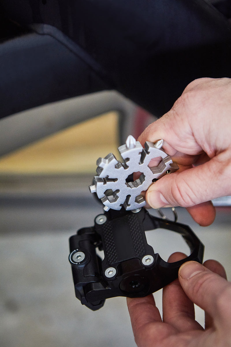 A person holds a Snowflake Tool and a bicycle pedal, positioning the Snowflake Tool near the pedal for maintenance or adjustment.