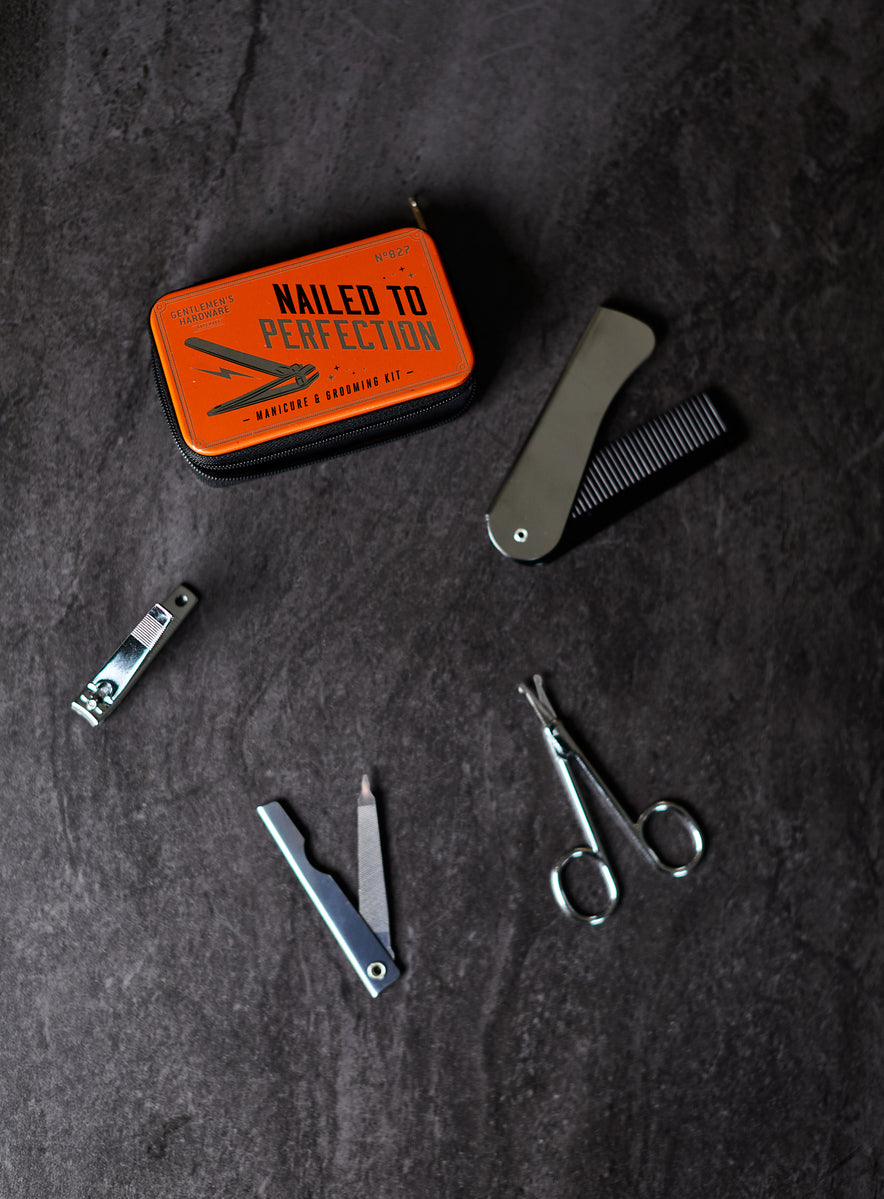 A Manicure Kit on a dark surface, featuring a metal comb, nail clippers, tweezers, scissors, and an orange tin labeled Nailed to Perfection.