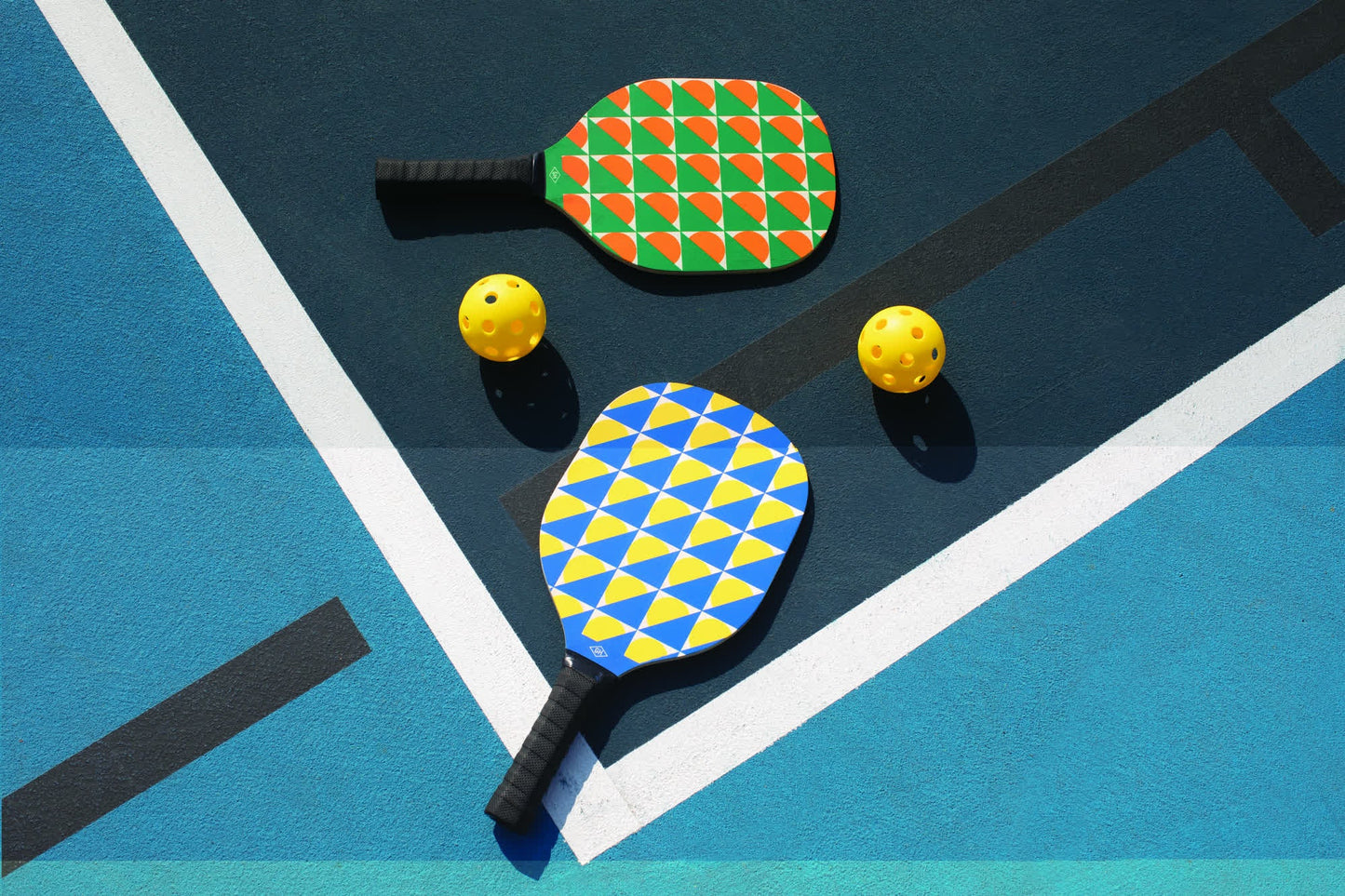 The Pickle Ball Set includes two colorful paddles and two yellow perforated balls, displayed on a blue outdoor court—perfect for exciting games and friendly competition.