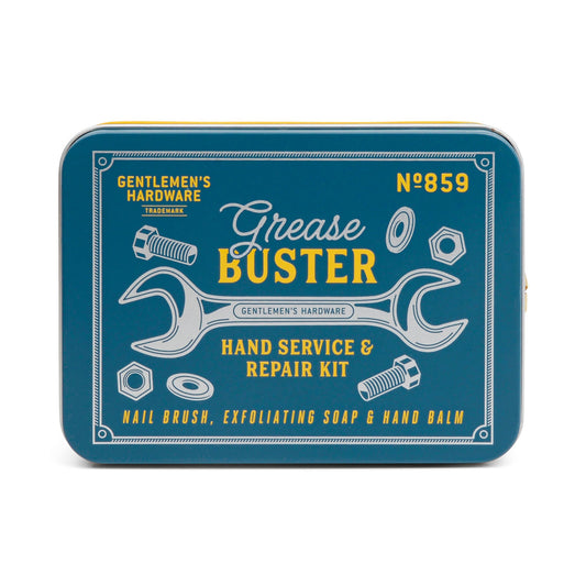 A blue metal tin labeled Grease Busters Hand Care Kit, decorated with wrench, nuts, and bolts illustrations, contains Exfoliating Soap, a Nail Brush, and nourishing Hand Balm.