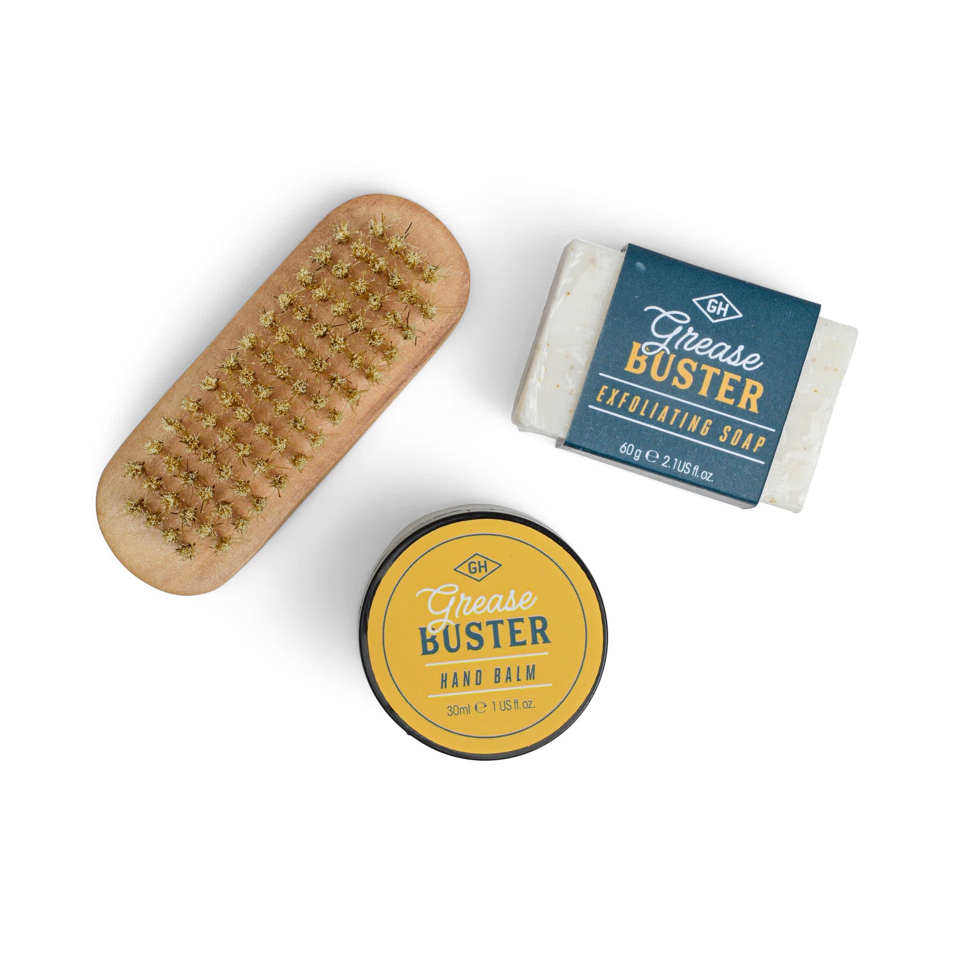 The Grease Busters Hand Care Kit, featuring a wooden nail brush, a tin of Grease Buster Hand Balm, and a bar of Grease Buster Exfoliating Soap, is neatly arranged on a white background.