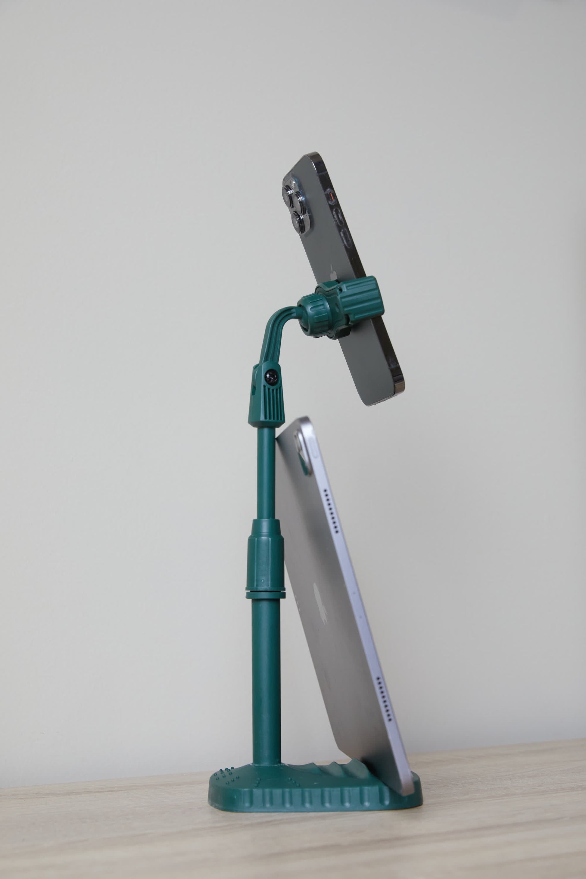 The Phone Tripod is a green desk companion that keeps your smartphone upright and supports your tablet at an angle on a light surface with a plain background.