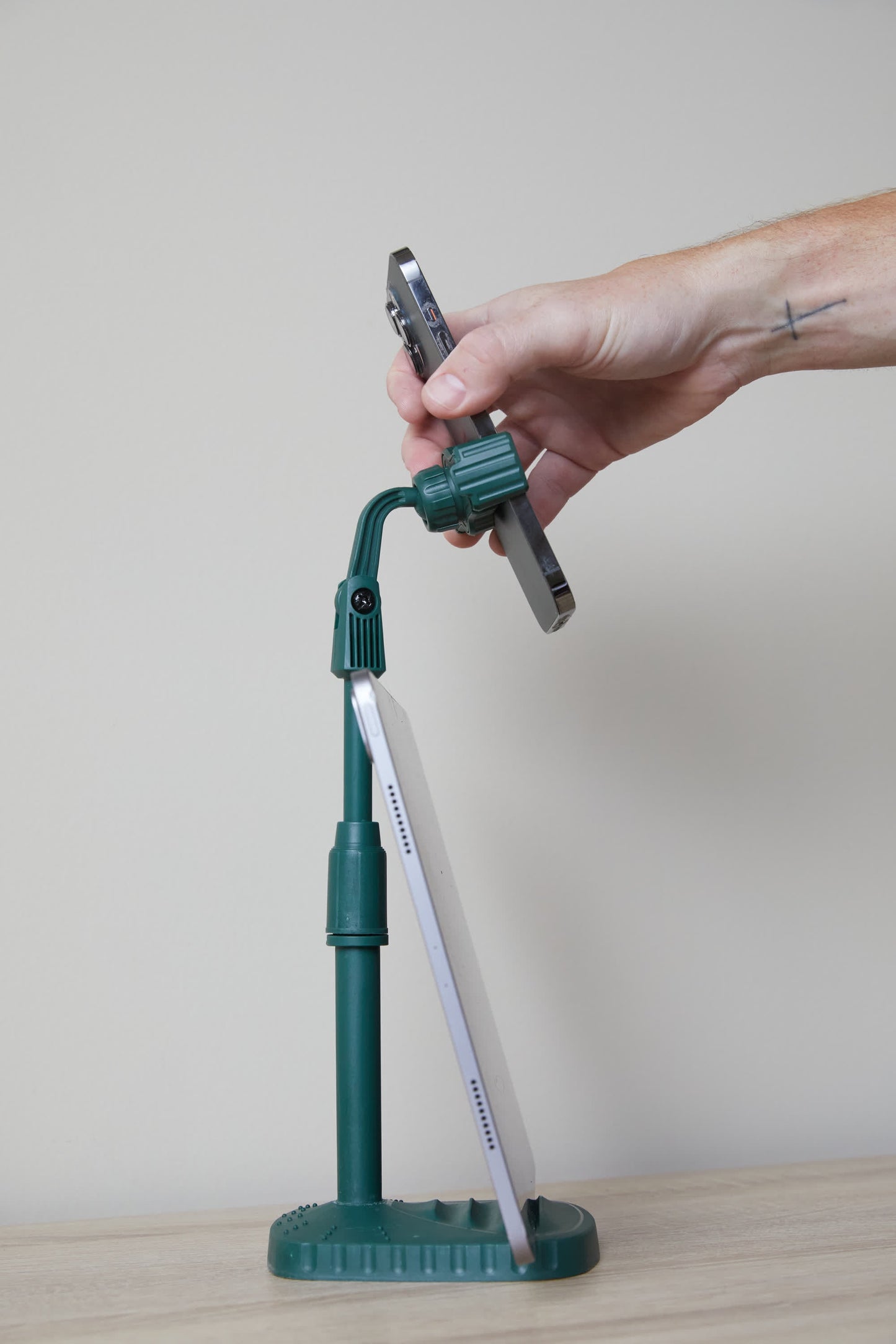 A hand adjusts a smartphone on the Phone Tripod, which also supports a tablet vertically against a plain background—a perfect desk companion.