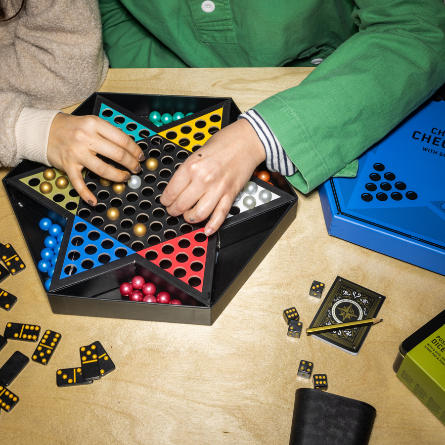 Two hands of humans each reaching for the pieces on a Chinese Checkers board 