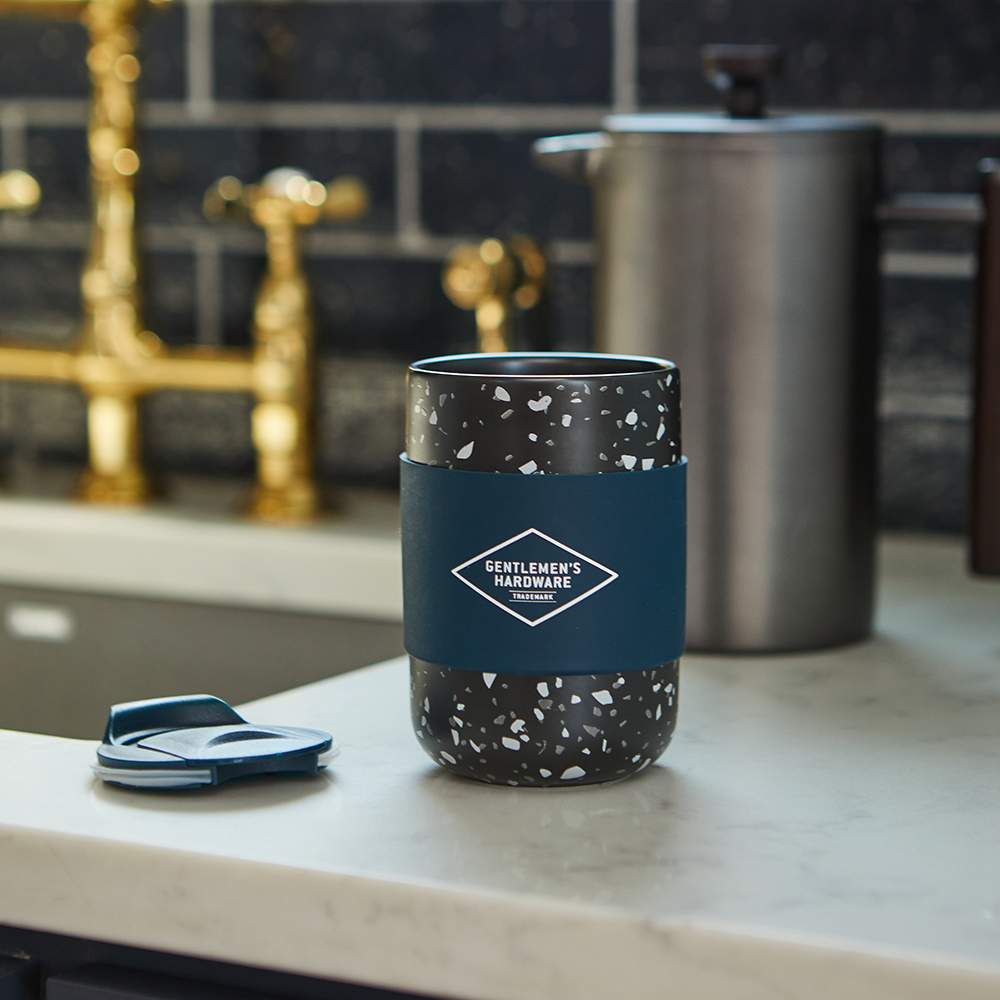 A black and white speckled Ceramic Travel Coffee Mug 13.5 oz sits on a kitchen counter with its lid beside it.