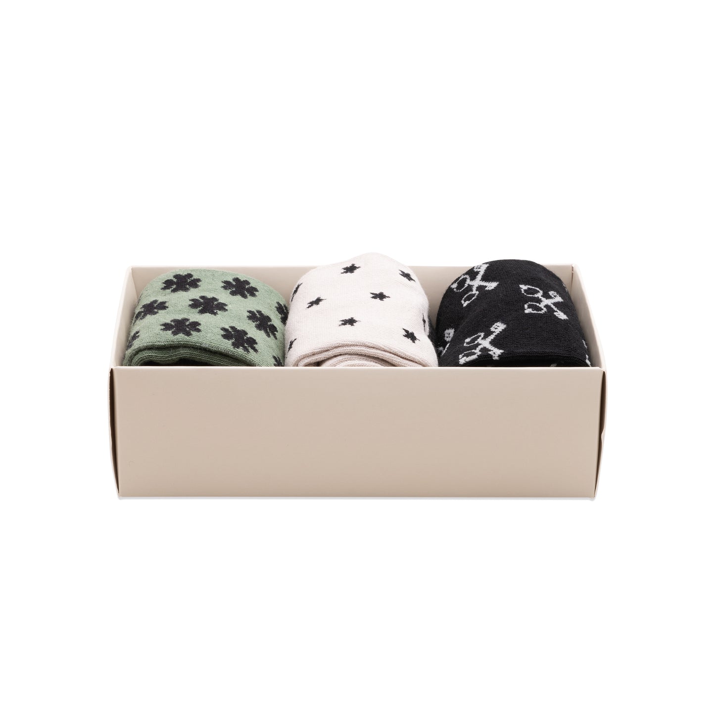 The Lucky Socks - 3 Pack includes three pairs in a beige box: green with black flowers, white with black stars, and black with white keys and lucky icons, all crafted from soft combed cotton.