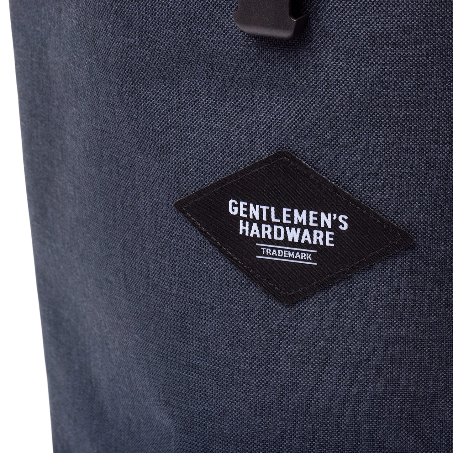 Close-up of the Insulated Cooler Backpack, dark fabric with a black diamond-shaped patch labeled Gentlemens Hardware Trademark in white.