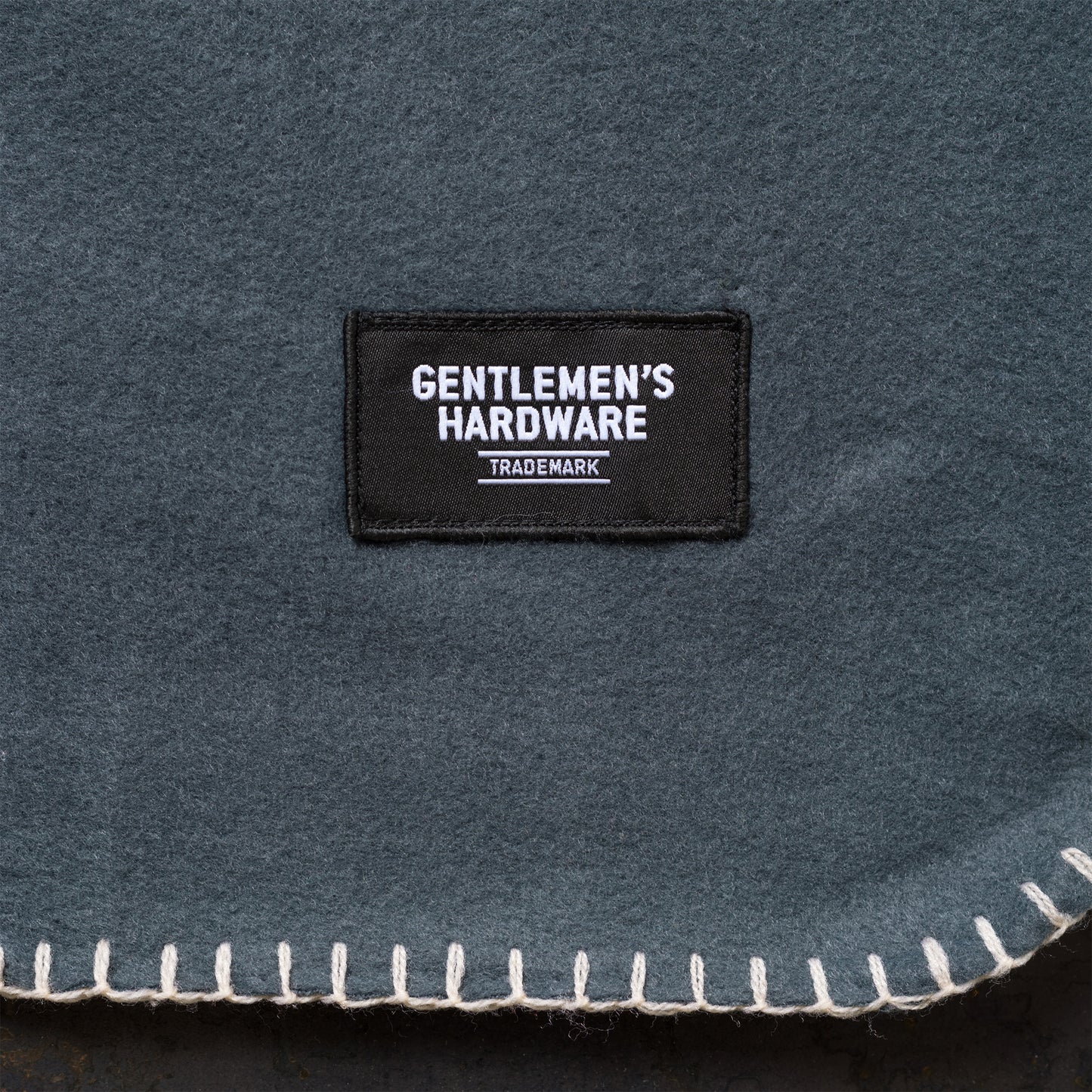 The Camping Blanket is a lightweight, dark grey fabric with stitched edges and a rectangular black patch labeled Gentlemen’s Hardware Trademark in white—ideal for outdoor adventures.