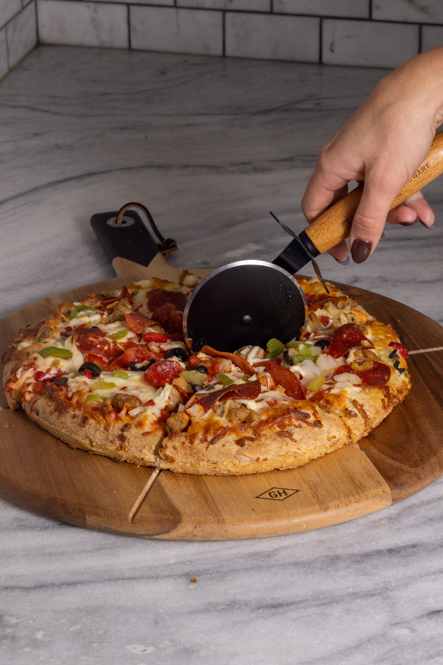 Female hand cutting the pizza on the serving board with the Gentlemen's Hardware pizza cutter