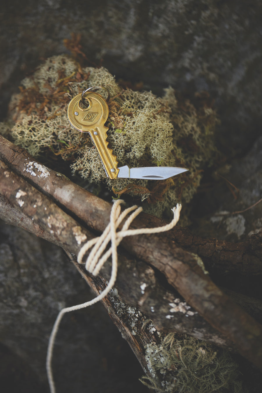 Key Pocket Knife resting on moss next to twigs bound by twine