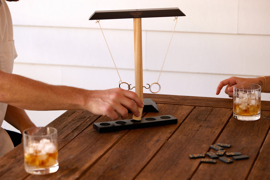 Ring Swing Game on a picnic table with rocks glasses and dominoes while two people play