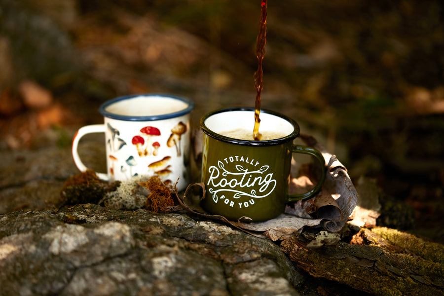 Enamel Mug - Rooting For You 17 fl oz next to the Mushroom enamel mug on rocks in the wilderness